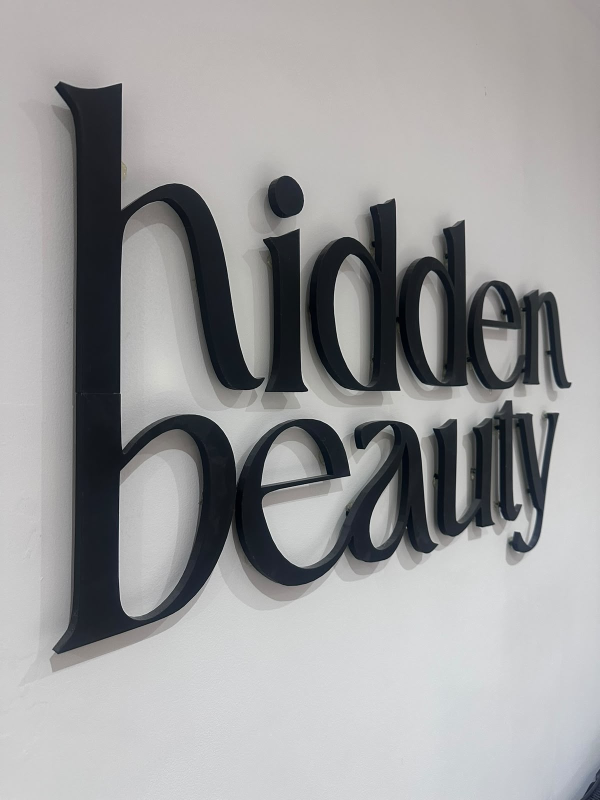 The Hidden Beauty wordmark in raised black lettering on the studio wall