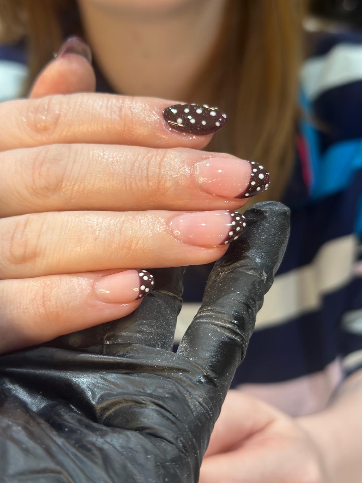 A dark French tip manicure finished with fine white dots