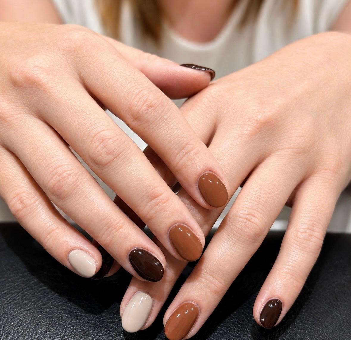 A gel manicure in mixed nude, tan and chocolate brown tones, a different shade on each nail